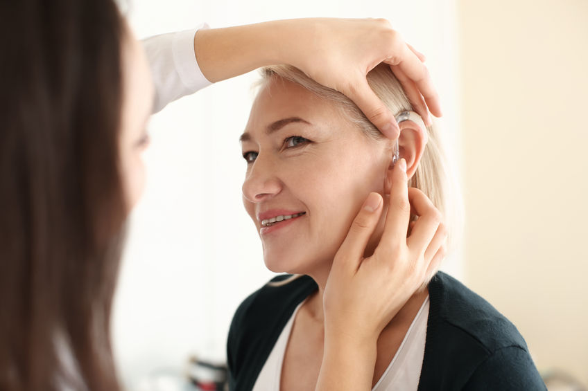Doctor putting hearing aid in woman's ear