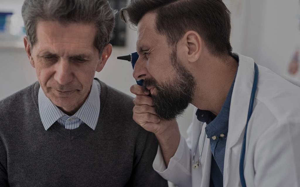Audiologist examining an ear of an older male patient